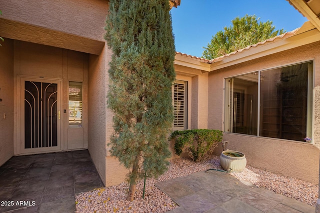 entrance to property with stucco siding, a tiled roof, and a patio