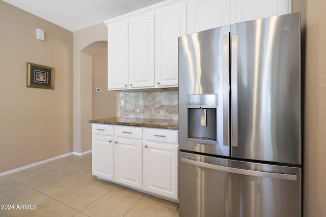 kitchen with light tile patterned flooring, white cabinets, backsplash, dark stone countertops, and stainless steel fridge