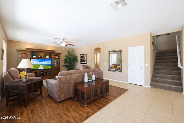 living area with arched walkways, light tile patterned flooring, visible vents, a ceiling fan, and stairway