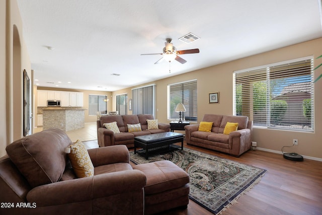 living room featuring ceiling fan, baseboards, visible vents, and light wood-style floors