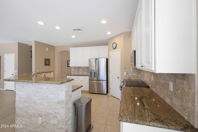 kitchen featuring arched walkways, a center island with sink, stainless steel appliances, visible vents, and white cabinets