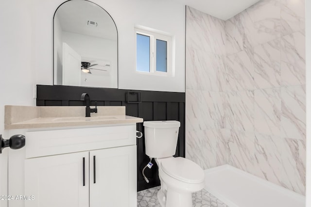 bathroom with ceiling fan, tiled shower, vanity, and toilet