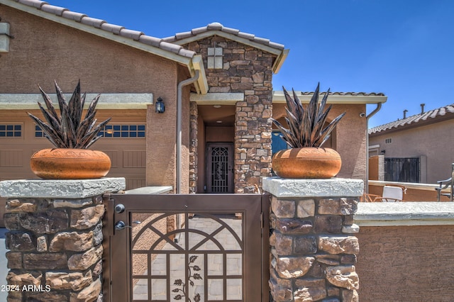 property entrance featuring an attached garage, a tiled roof, stone siding, a gate, and stucco siding