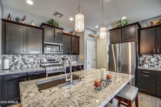 kitchen featuring dark brown cabinetry, visible vents, appliances with stainless steel finishes, a breakfast bar, and hanging light fixtures