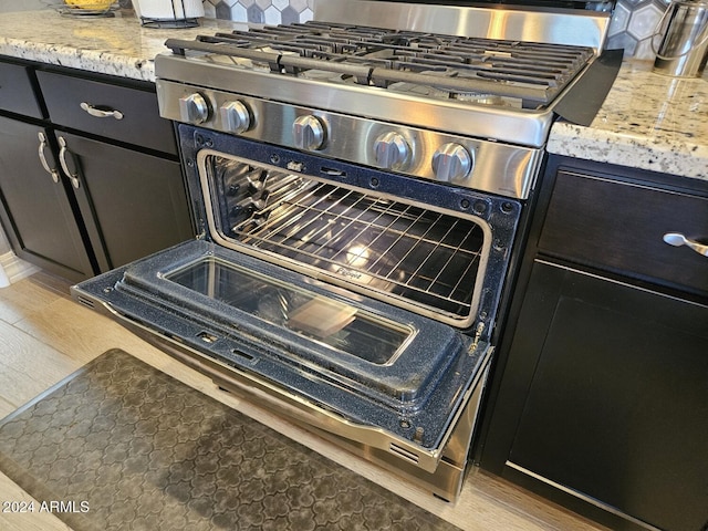 room details with light stone countertops, gas range, dark cabinets, and backsplash