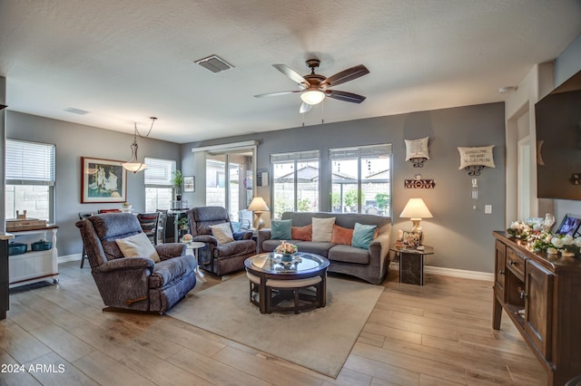 living area featuring a textured ceiling, light wood finished floors, visible vents, and baseboards