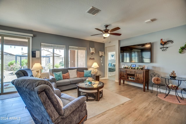 living area with visible vents, light wood-style flooring, ceiling fan, a textured ceiling, and baseboards