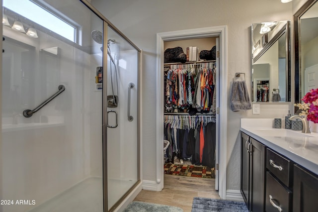 bathroom featuring a shower stall, a walk in closet, wood finished floors, and vanity