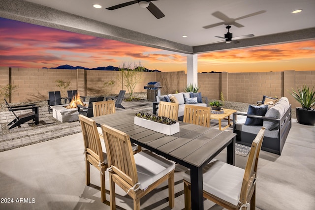 patio terrace at dusk featuring ceiling fan and an outdoor living space with a fire pit