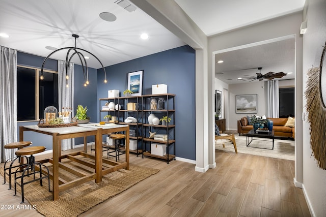 dining room with ceiling fan with notable chandelier and light hardwood / wood-style flooring