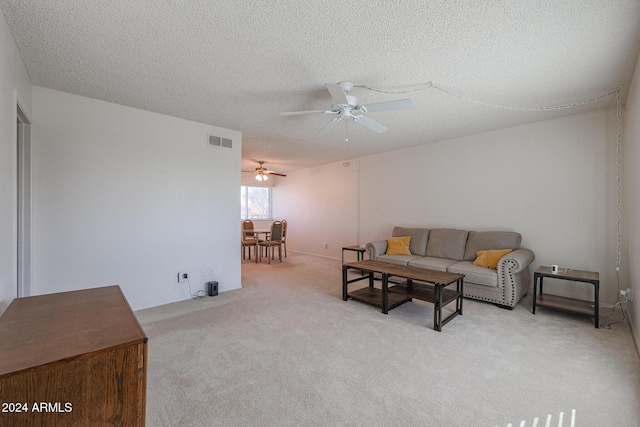 living room featuring ceiling fan, light colored carpet, and a textured ceiling