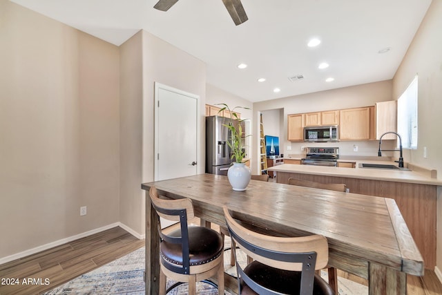 kitchen with light brown cabinets, sink, kitchen peninsula, stainless steel appliances, and light hardwood / wood-style floors