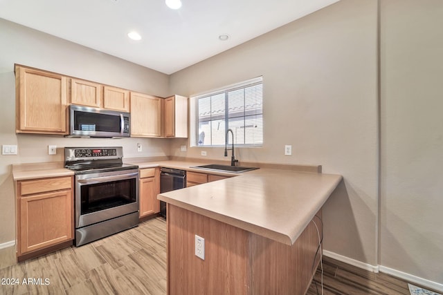 kitchen featuring appliances with stainless steel finishes, light wood-type flooring, sink, and kitchen peninsula