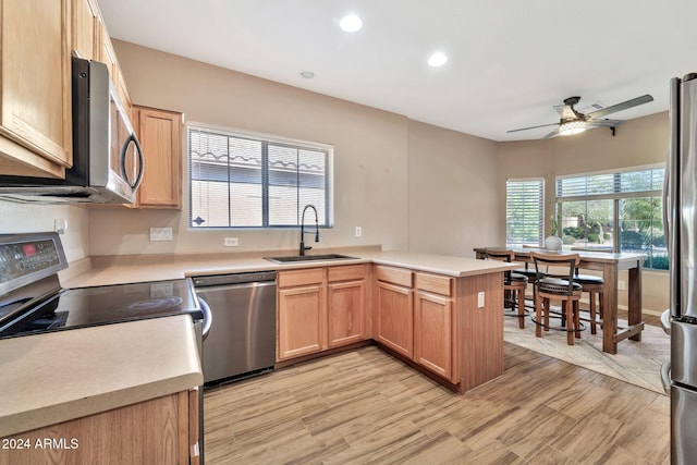 kitchen with light wood-type flooring, ceiling fan, sink, kitchen peninsula, and appliances with stainless steel finishes