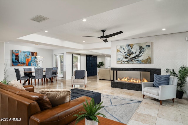 living room with a tile fireplace, a tray ceiling, and ceiling fan