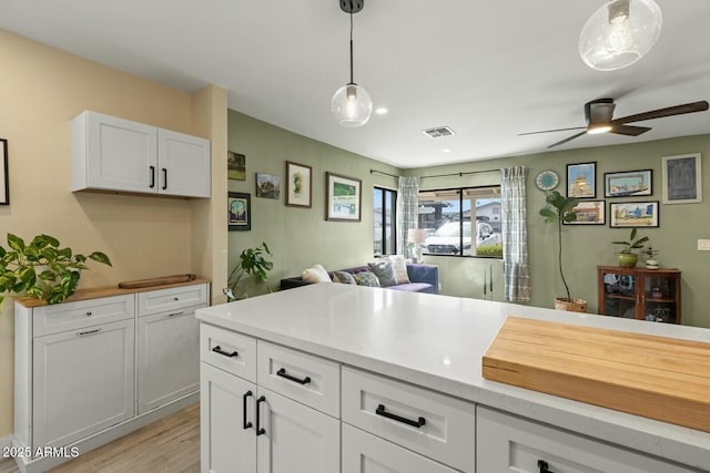 kitchen featuring a ceiling fan, visible vents, light countertops, white cabinets, and decorative light fixtures