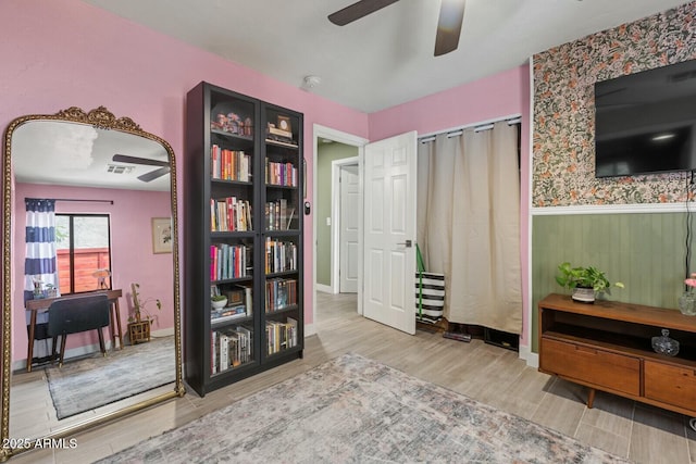 interior space with a wainscoted wall, wood finished floors, a ceiling fan, and visible vents