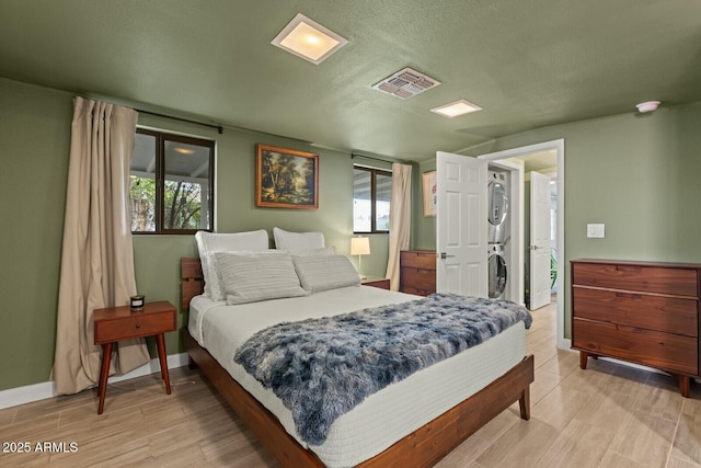 bedroom featuring visible vents, multiple windows, stacked washer and dryer, and baseboards