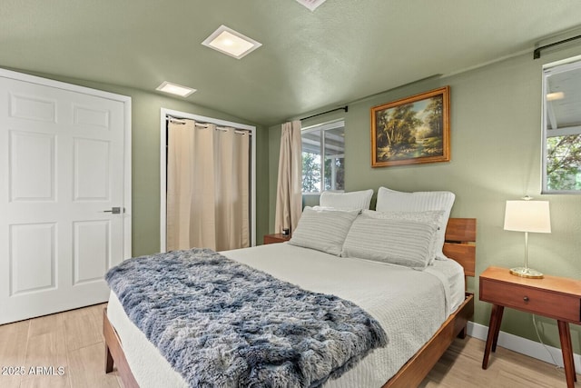 bedroom with light wood finished floors, baseboards, and vaulted ceiling