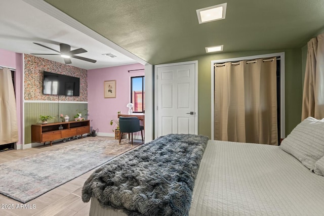 bedroom with a textured ceiling, wood finished floors, visible vents, and wainscoting