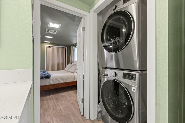 laundry room featuring light wood-type flooring, visible vents, laundry area, and stacked washing maching and dryer