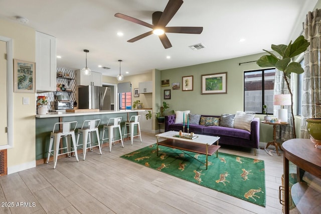 living room featuring a wealth of natural light, visible vents, light wood-type flooring, and a ceiling fan