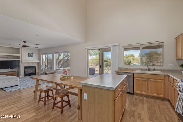 kitchen featuring a tile fireplace, ceiling fan, a sink, light wood-style floors, and stainless steel dishwasher