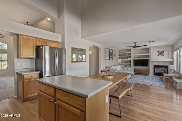 kitchen with a kitchen island, a ceiling fan, arched walkways, light wood-style floors, and freestanding refrigerator