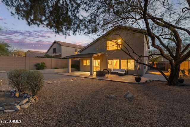 back of property at dusk with a fenced backyard, an outdoor hangout area, stucco siding, and a patio area