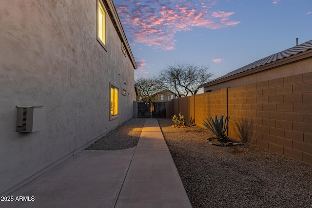 property exterior at dusk with a fenced backyard, a gate, a patio, and stucco siding