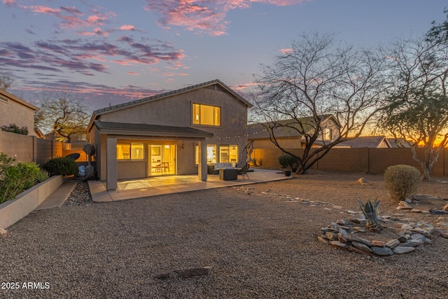 back of property at dusk featuring a fenced backyard, stucco siding, and a patio