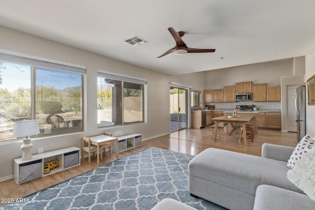 living area featuring light wood finished floors, baseboards, visible vents, and ceiling fan