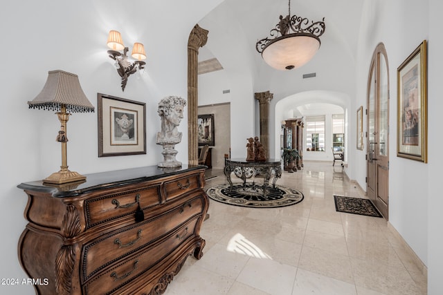 foyer entrance featuring light tile patterned flooring, a high ceiling, and decorative columns