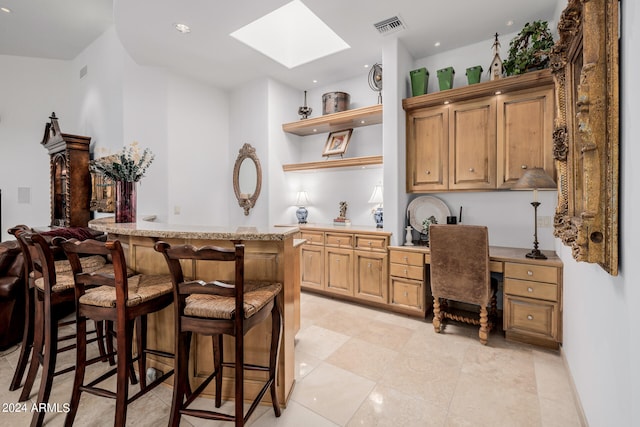 kitchen with a skylight, built in desk, a kitchen bar, and light tile patterned flooring