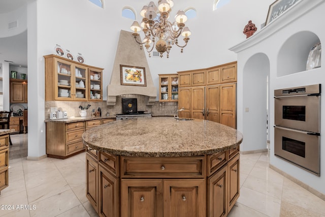 kitchen featuring a towering ceiling, light stone countertops, an island with sink, and appliances with stainless steel finishes