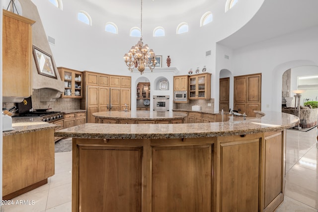 kitchen featuring a large island with sink, stainless steel appliances, a high ceiling, hanging light fixtures, and light tile patterned floors