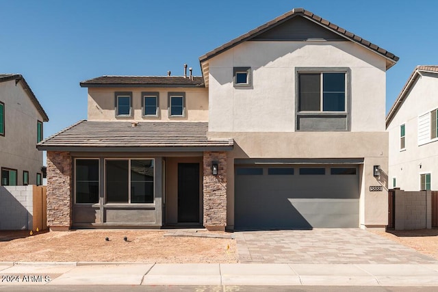 view of front facade featuring decorative driveway, fence, an attached garage, and stucco siding