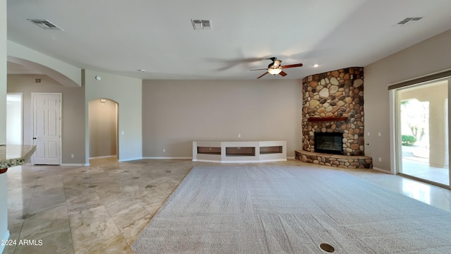 unfurnished living room featuring a stone fireplace and ceiling fan