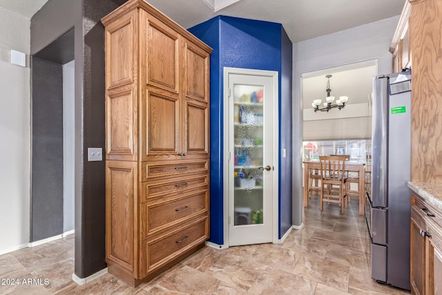 kitchen with a chandelier, stainless steel fridge, decorative light fixtures, and light stone counters