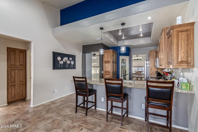 kitchen featuring hanging light fixtures, a raised ceiling, light stone counters, kitchen peninsula, and a breakfast bar area