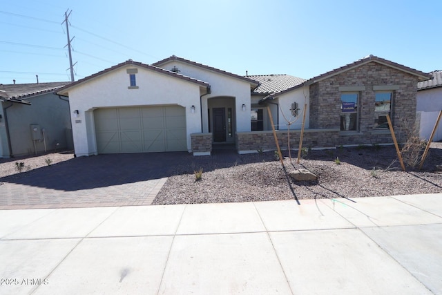 view of front facade featuring stucco siding, stone siding, a tiled roof, decorative driveway, and a garage