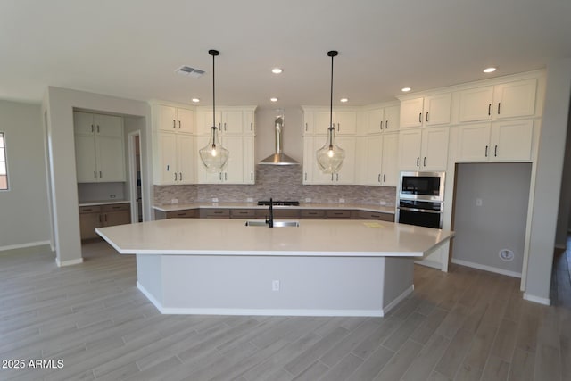 kitchen with a sink, stainless steel appliances, wall chimney range hood, visible vents, and decorative backsplash