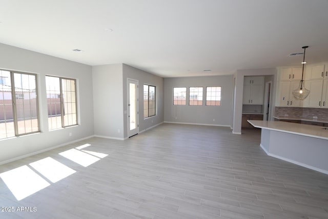 unfurnished living room featuring baseboards, visible vents, and light wood finished floors