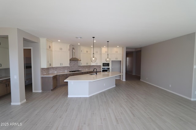 kitchen with light countertops, wall chimney exhaust hood, tasteful backsplash, light wood-style flooring, and stainless steel appliances