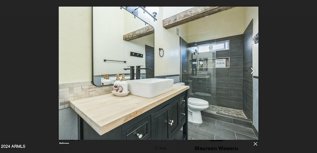 bathroom featuring tile patterned floors, vanity, tiled shower, tile walls, and toilet