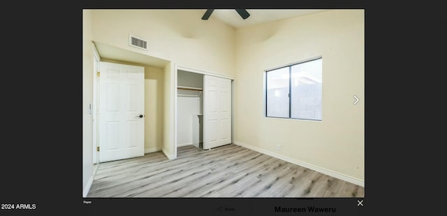 unfurnished bedroom with a high ceiling, light wood-type flooring, a closet, and ceiling fan