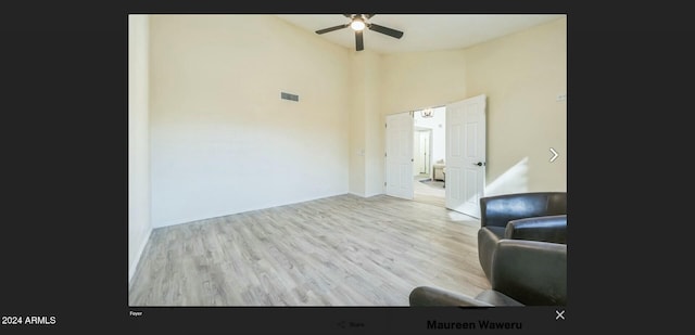 living room with ceiling fan, a high ceiling, and light hardwood / wood-style flooring