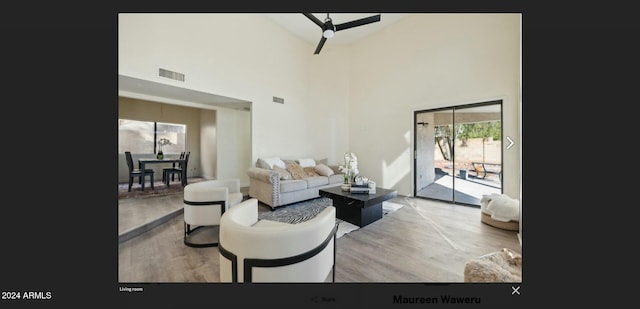 living room featuring ceiling fan, light hardwood / wood-style flooring, and a towering ceiling