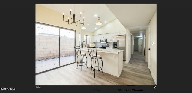 kitchen featuring stainless steel appliances, hanging light fixtures, a breakfast bar, white cabinets, and light wood-type flooring