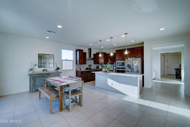 kitchen featuring pendant lighting, light tile patterned floors, wall chimney exhaust hood, appliances with stainless steel finishes, and decorative backsplash